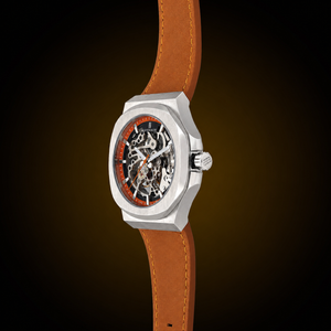 A skeleton watch with a silver-toned case, a brown leather strap, and a black dial with orange accents, shown against a dark brown gradient background.