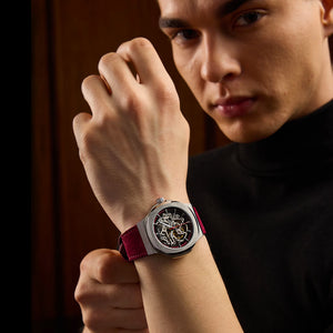 Man wearing a watch with a red strap on his wrist, against a dark background