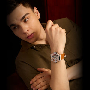 Man wearing a watch with a brown strap and brown shirt against a dark background